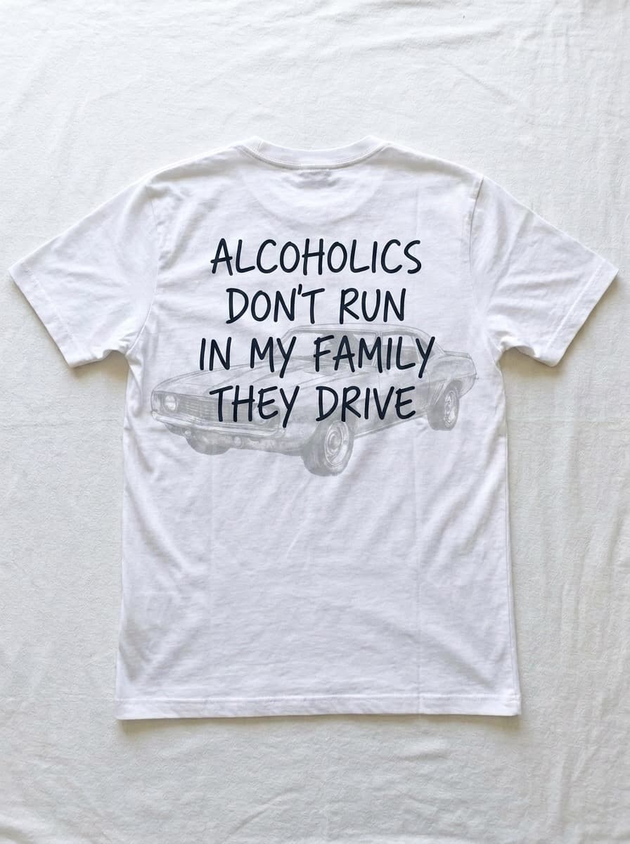 Back of a white t-shirt printed with alcoholics don't run in my family they drive over a faint line drawing of a parked muscle car.